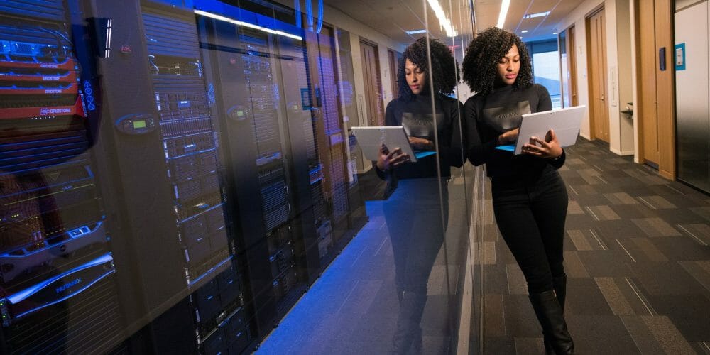 Woman leaning on glass in front of rows of computer servers