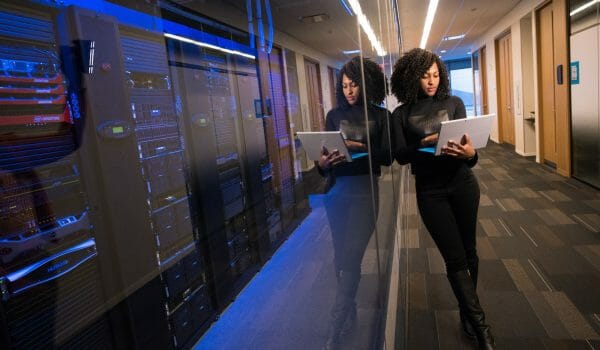 Woman leaning on glass in front of rows of computer servers